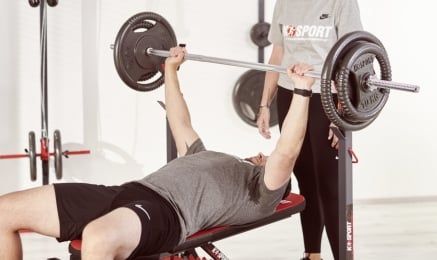Athlet beim Bankdrücken mit Langhantel und Spotter im K-Sport Homegym