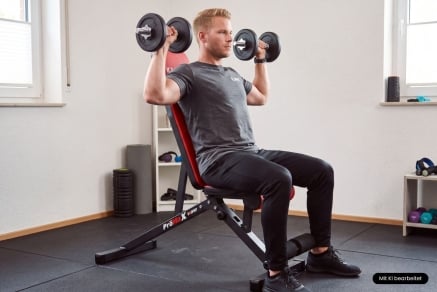 Athlet beim sitzenden Schulterdrücken mit Kurzhanteln auf einer K-Sport-Hantelbank im Homegym