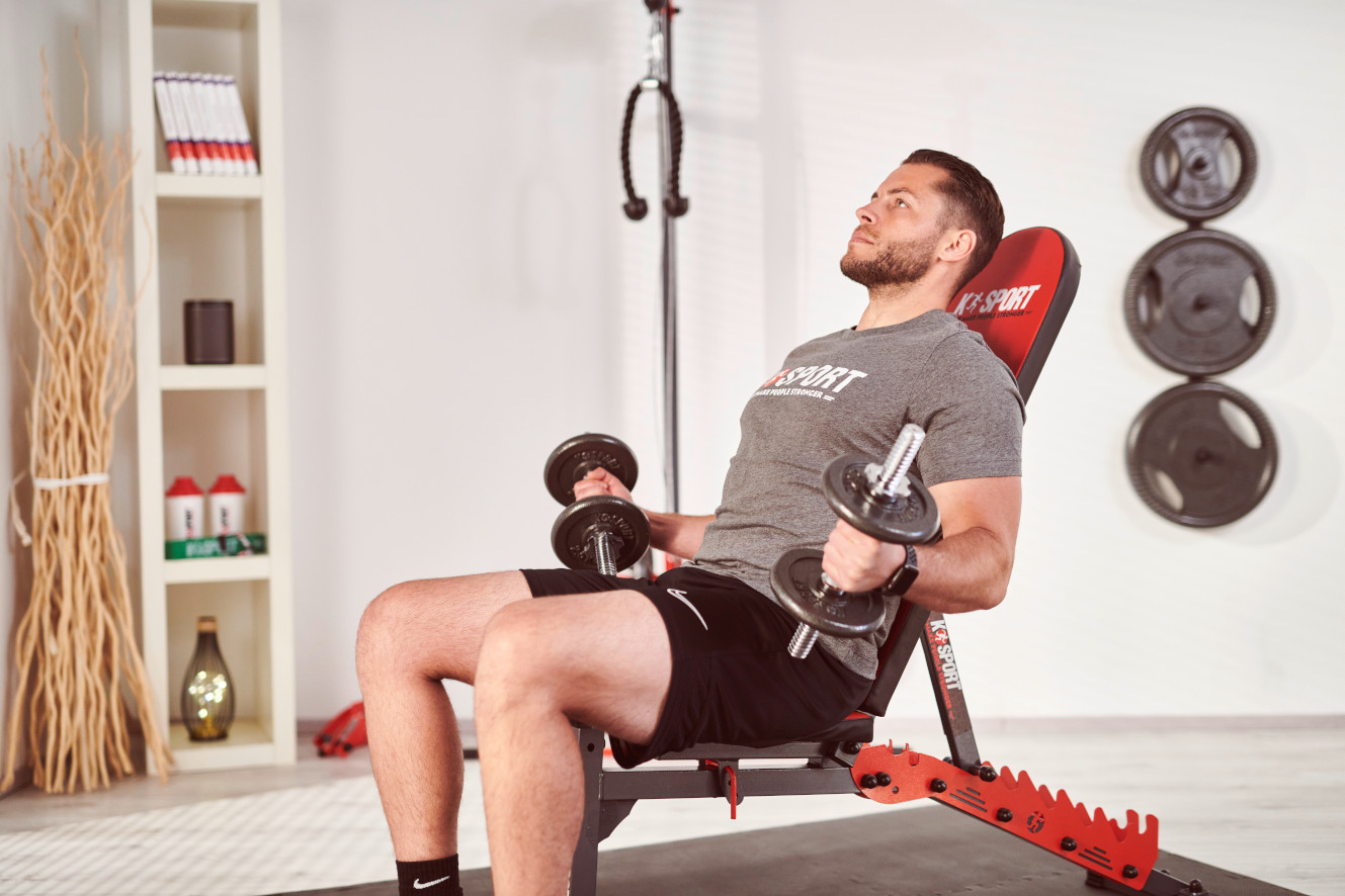 Mann trainiert seinen Bizeps mit Kurzhanteln auf einer Schrägbank im Fitnessraum.