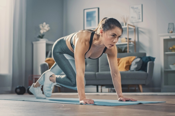 Vrouw traint gemotiveerd thuis na de vakantie – herstart van fitness met oefeningen met het eigen lichaamsgewicht