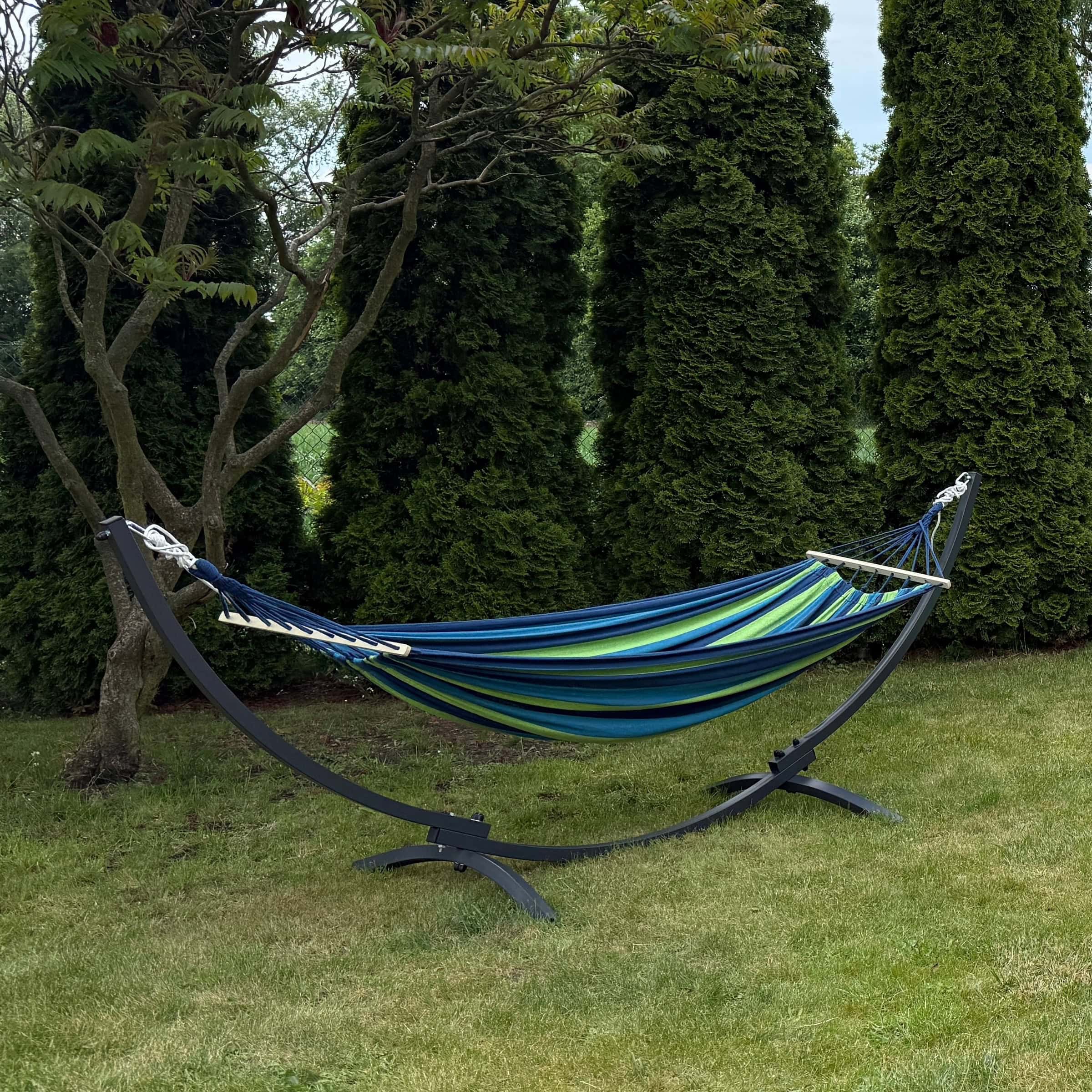 Amaca da giardino con struttura in metallo nera su prato sotto alberi ombrosi