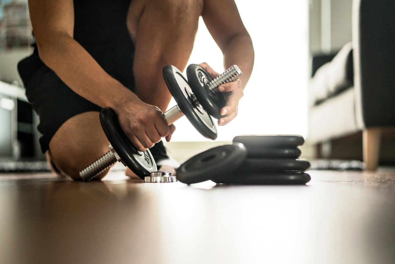 Persona che assembla un bilanciere con diversi dischi, concentrata sulle mani e sul bilanciere, su un pavimento di una sala fitness