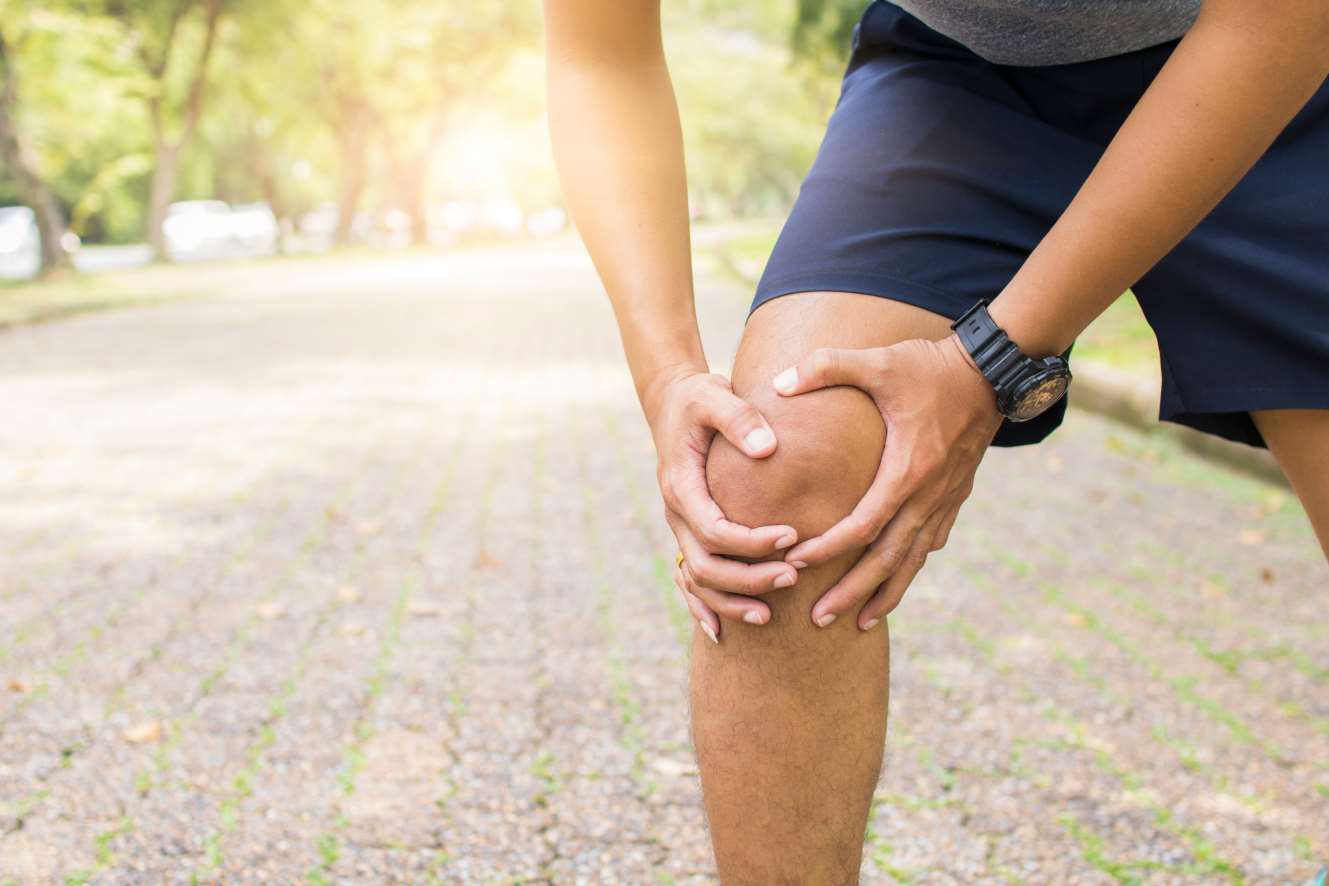 Un uomo si tiene il ginocchio dolorante durante lo sport all'aperto