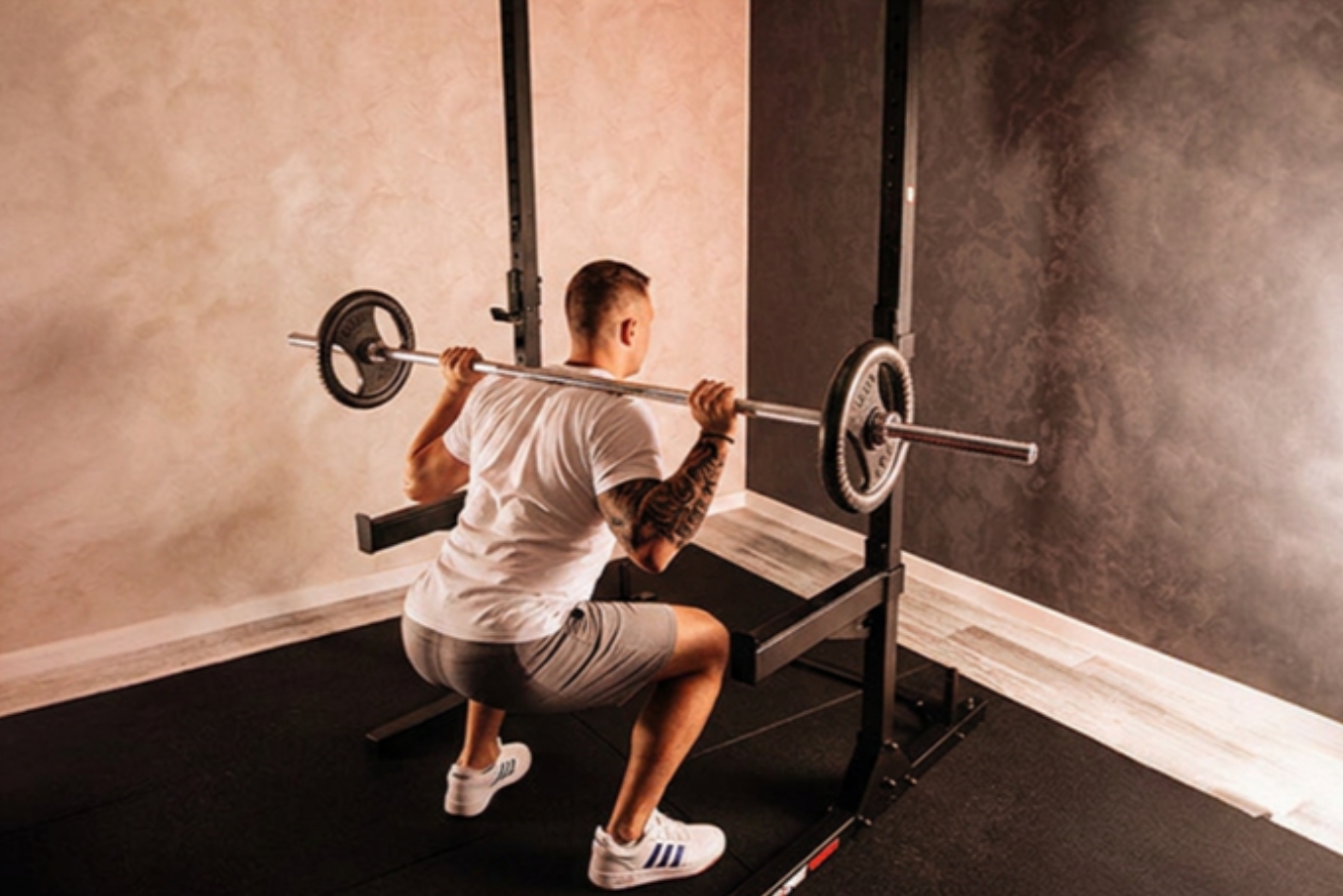 Man voert squats uit met een halterstang in een stabiel squat rack voor effectieve beentraining thuis.