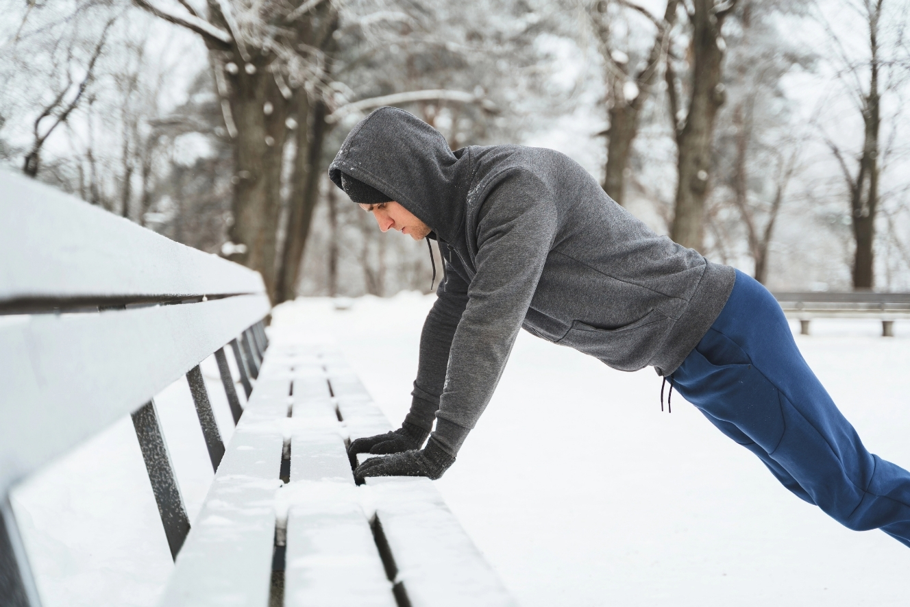 Man doet push-ups op een parkbank in de sneeuw en overwint de winterdip tijdens het trainen